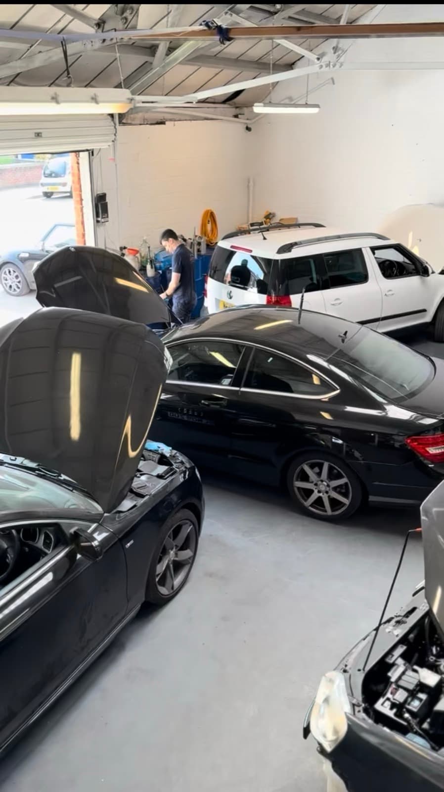 A wide view of the working bay, with vehicles in and the roller door open to the street.