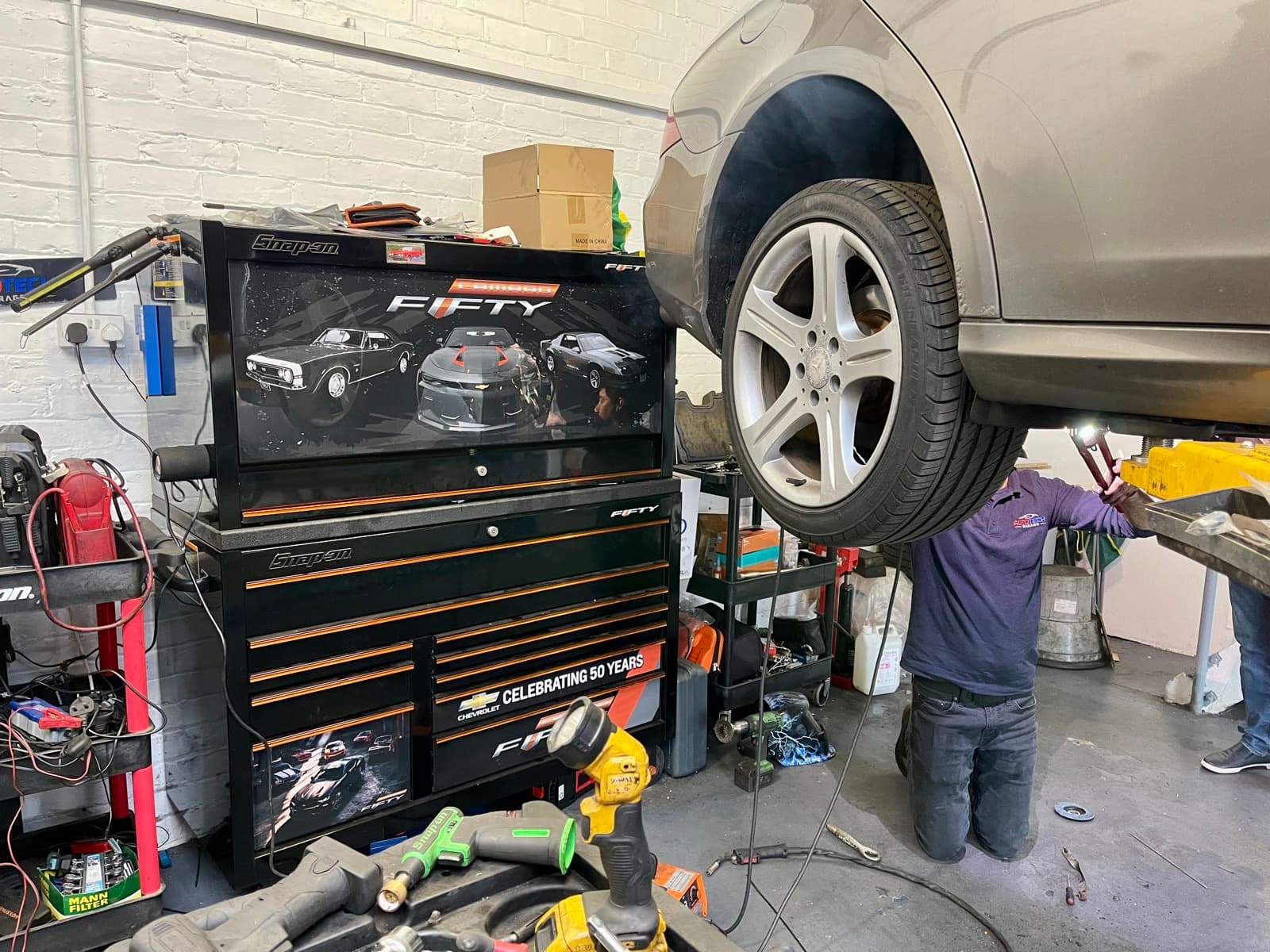 The workshop interior, with a car raised on the ramp and a technician working underneath it.