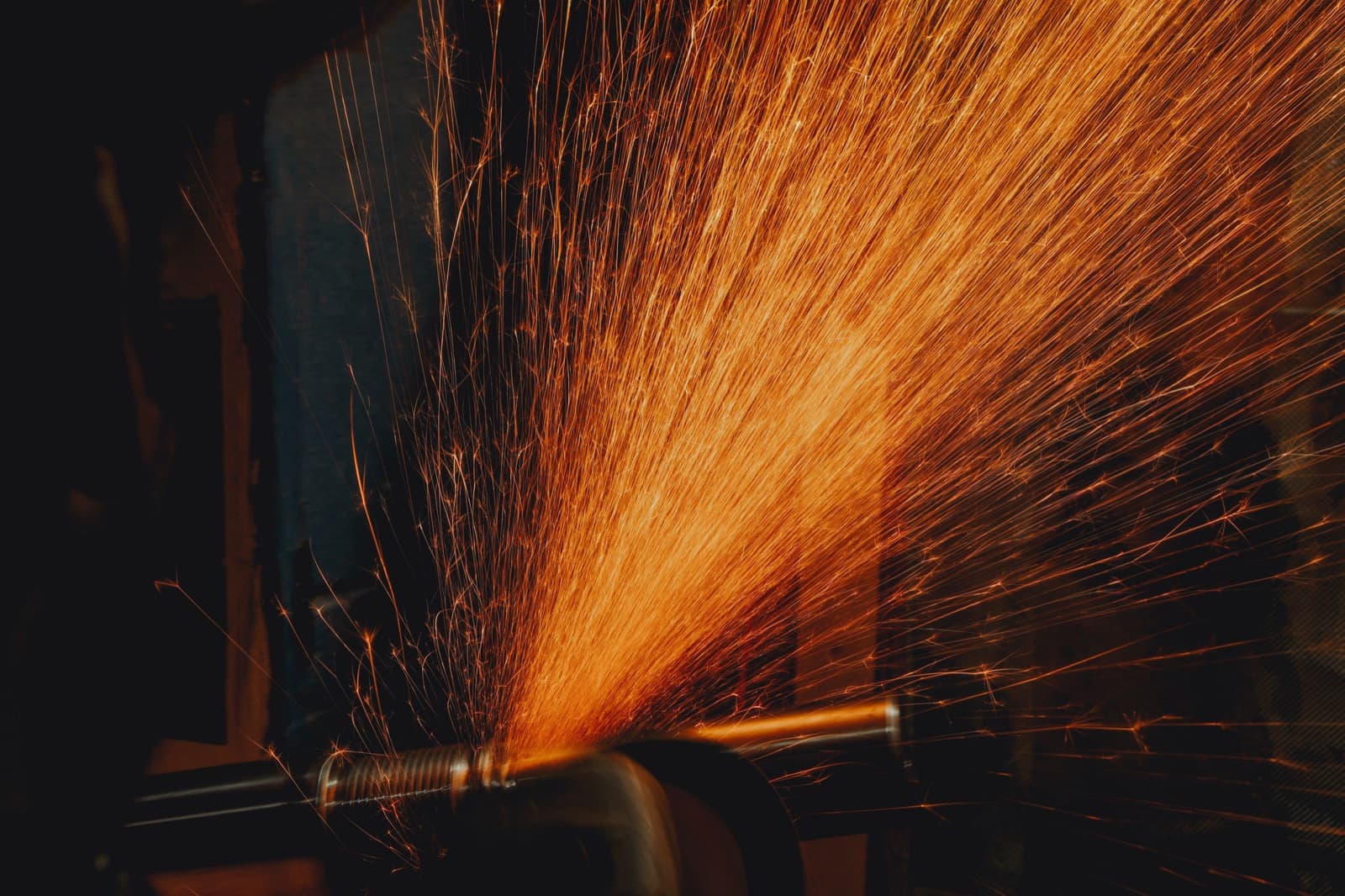 A plume of orange sparks thrown off a length of threaded steel bar clamped in a bench vice as it is cut.